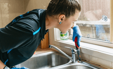 Cleaner scrubbing a kitchen sink faucet