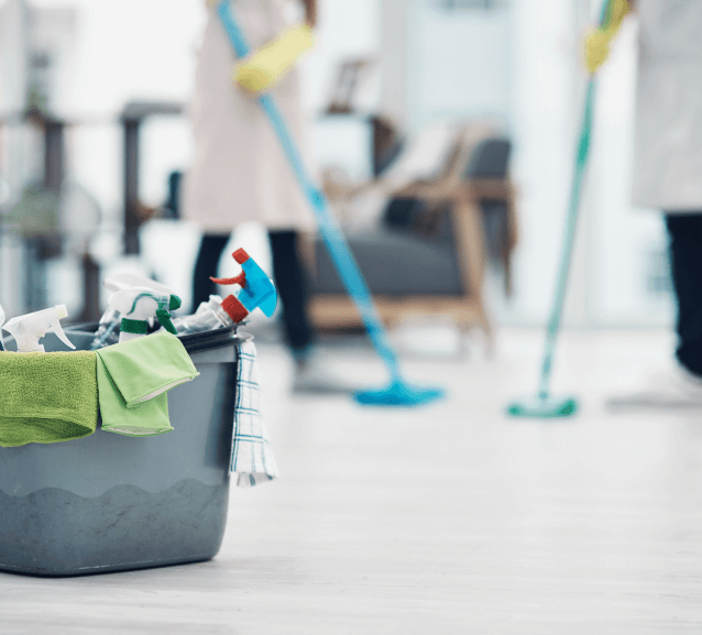 Cleaning supplies in a bucket with cleaners mopping an office floor